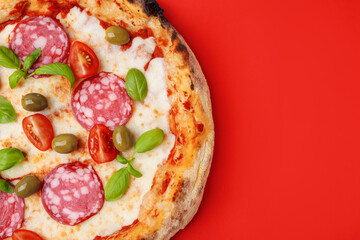 Delicious pizza with salami, olives, tomatoes and basil on red table, top view. Space for text