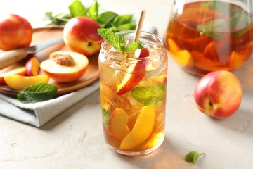 Refreshing iced peach tea with mint and fresh fruits on white table, closeup
