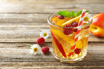 Refreshing ice tea with peach, raspberries and chamomiles on wooden table, closeup. Space for text
