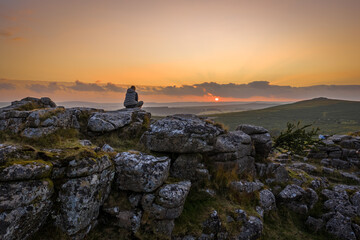 Family hiking on Dartmoor tors at sunset, silhouetted against dramatic skies in scenic moorland landscape