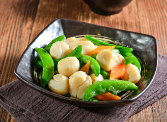 Sautéed scallops with vibrant green snow peas and carrots in bowl side view of Asian seafood