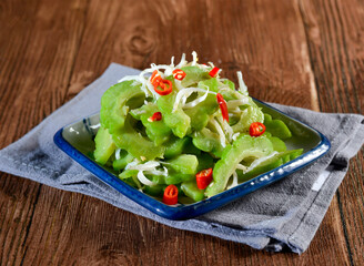 Stir fried bitter melon with anchovies and shredded ginger in plate side view of vibrant Asian dish