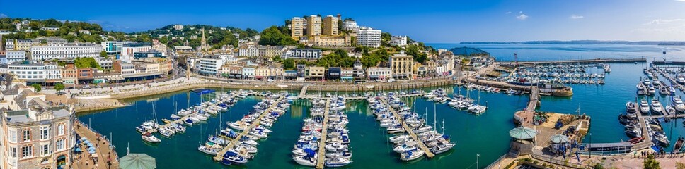 Aerial view of Torquay Marina on a sunny day, featuring yachts, boats, promenade, and blue sea along the English Riviera coastline