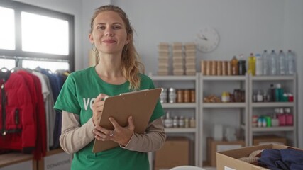 Woman with clipboard writing in warehouse as volunteer blonde young smiling during donation sorting items on shelves. - Powered by Adobe