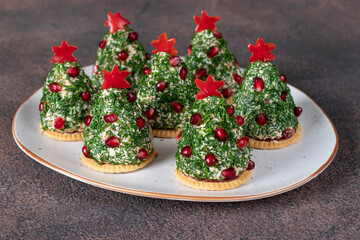 Festive snack on crackers in form of Christmas tree made of melted cheese, pomegranate, dill and stars from red pepper