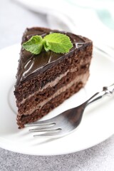 Piece of delicious chocolate cake with mint and fork on grey table, closeup