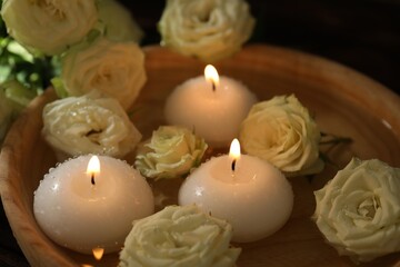 Burning candles, water and rose flowers in wooden bowl on table, closeup
