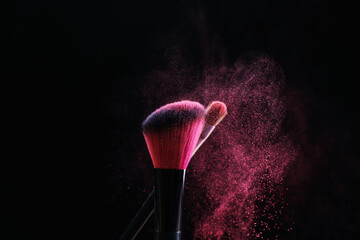 Makeup brushes with pink eye shadow on black background, closeup
