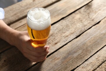 Man with glass of beer at wooden table, closeup. Space for text