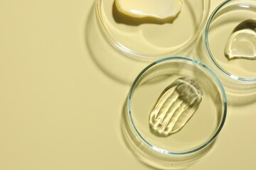 Different cosmetic products in Petri dishes on pale yellow background, flat lay. Space for text