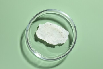 Cosmetic product in Petri dish on green background, top view
