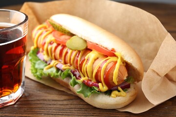 Tasty hot dog and soda drink on wooden table, closeup