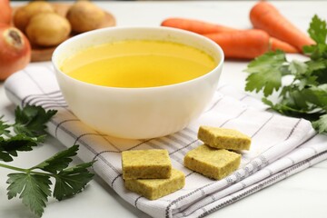 Aromatic bouillon cubes, broth, parsley and vegetables on white table, closeup