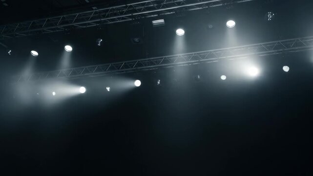 Stage Lighting Beams in Dark Venue - Multiple spotlights are mounted on a metal truss above a dark stage, casting beams of light downward.