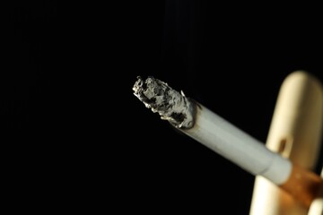 Wooden hand figure with burning cigarette on black background, closeup. Space for text