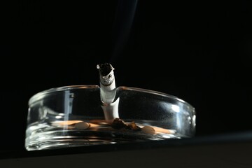 Cigarette butts in ashtray on black background, closeup