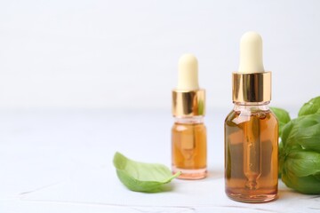 Bottles of aromatic essential oils and herbs on white textured table, closeup. Space for text