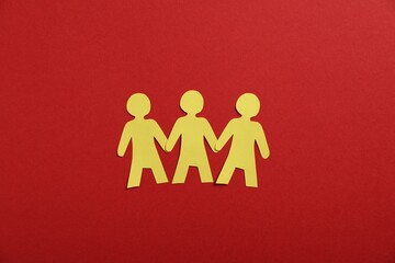 Human paper figures holding hands on red background, flat lay