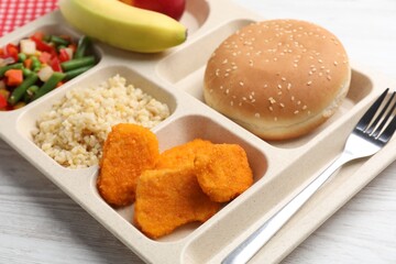 Plastic tray with tasty food and fork on light wooden table, closeup. School lunch