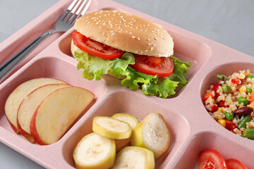 Plastic tray with tasty food and fork on grey table, closeup. School lunch