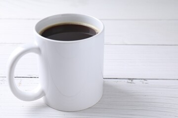 Tasty coffee in cup on white wooden table, closeup. Space for text