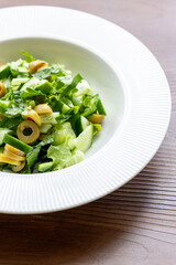 Mediterranean salad with green olives on white plate in close-up