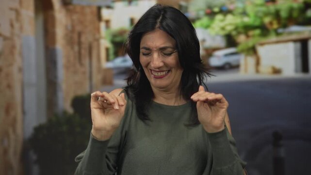Middle aged hispanic woman in olive top makes rejection gesture with hands on the cobblestone street of an old town; denial.