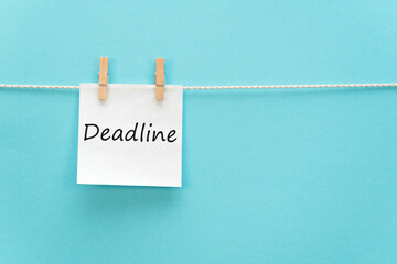 White sticker on a rope with a clothespin with an inscription - deadline. Blue background. No people.