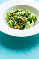 Mediterranean salad with green olives on white plate in close-up