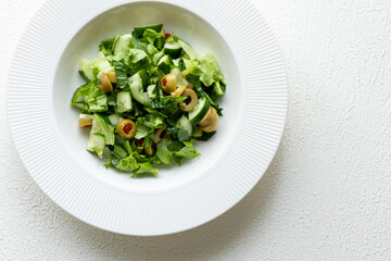 Mediterranean salad with green olives on white plate in close-up