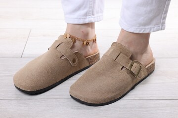 Woman in stylish beige slippers on light wooden floor, closeup