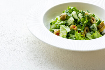 Mediterranean salad with green olives on white plate in close-up