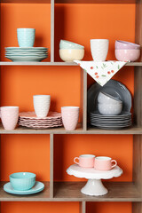 Shelving unit with different dishware and cups near orange wall indoors