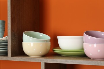 Different dishware on wooden shelf near orange wall indoors, closeup