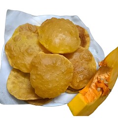 A plate of freshly fried golden pumpkin poori served on tissue, with a slice of raw pumpkin on the side, isolated on white.