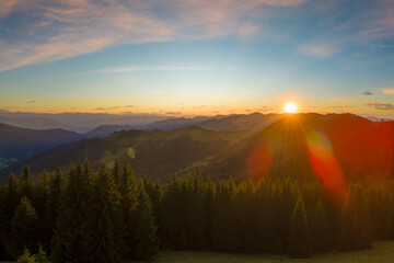 Aerial view of amazing mountain landscape. Bright colorful sunset in wild national park highlands. Dark spruce woods illuminated with yellow setting sun