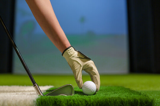 Golfer Hand with Glove Placing Ball on Artificial Turf in Indoor Golf Simulator Training Facility