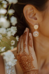 Elegant woman wearing gold earrings with henna art on hand. Beauty tradition concept.