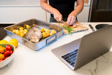 Woman Preparing Red Snapper Fish and Potatoes with Online Recipe Guidance at Home
