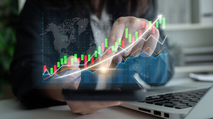 A business professional engages with financial data on a smartphone while analyzing stock market trends using digital graphs in a modern office environment. Impute