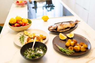 Grilled Snapper Fish with Lemon, Herbs, and Roasted Potatoes on Marble Kitchen Counter