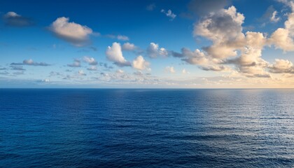 vast blue ocean meets clear sky with scattered white clouds at sunset for a serene natural seascape background