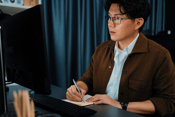 Smart businessman writing information from computer to check business data report on sales target revenue over late night time at modern office, focusing marketing creative project company. Infobahn.