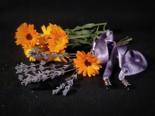 Fototapeta premium small bouquet of lavender with purple ribbon and calendula flowers on black background close-up