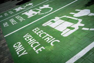 A vibrant green parking area clearly marked "ELECTRIC VEHICLE ONLY" with corresponding charging symbols, highlighting modern sustainable transportation infrastructure.