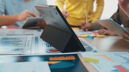 A dynamic office scene showing a diverse team engaged in a collaborative discussion around a table, featuring a digital tablet displaying data visualizations and charts. SACTR - Powered by Adobe