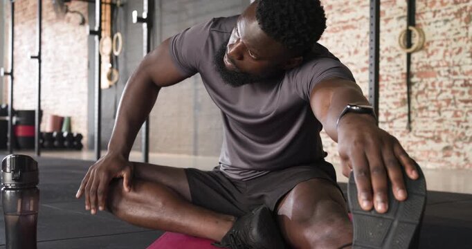 After workout man rolling massage ball under calf stretching hamstring on red mat at gym