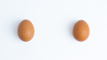 Two brown eggs on white background with copy space in the middle. Organic food, natural protein source, breakfast ingredient, healthy cooking, fresh farm produce, simple composition.
