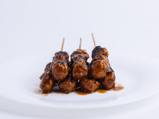 Grilled Indonesian meatball skewer with spicy peanut sauce on white plate. Asian street food, traditional snack, savory flavor, spicy dish, local cuisine, close-up, isolated.
