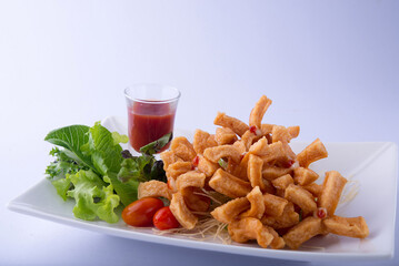 A golden-yellow fried sausage with a split end, green lettuce, red tomato, and red ketchup on a white plate, white background.